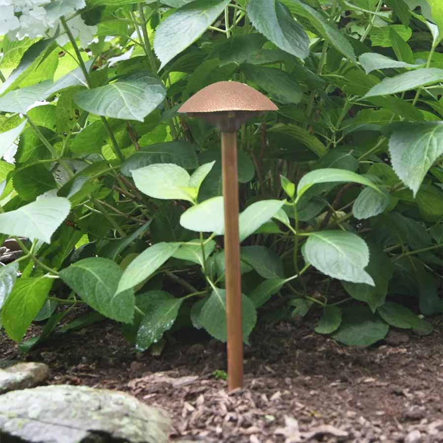 A CAST Craftsman Series bronze LED path light placed in a garden.