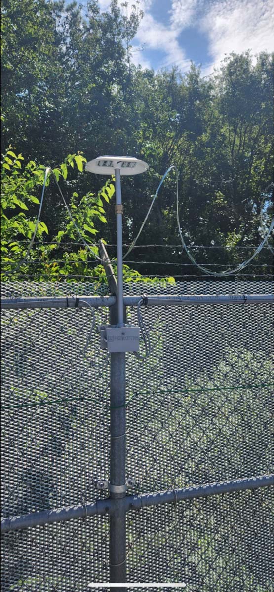 cast-light-mounted-to-barbed-wire-fence-in-daylight-with-trees
