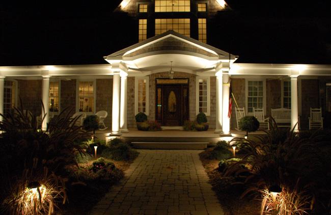 Clubhouse at night with lighting on porch and along center pathway made of stone.