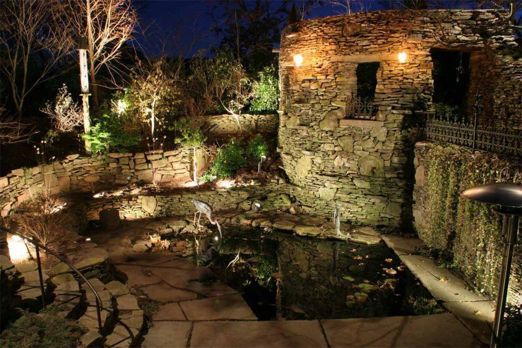 Rock wall grotto with lights over small pond with a bird drinking from it at night.