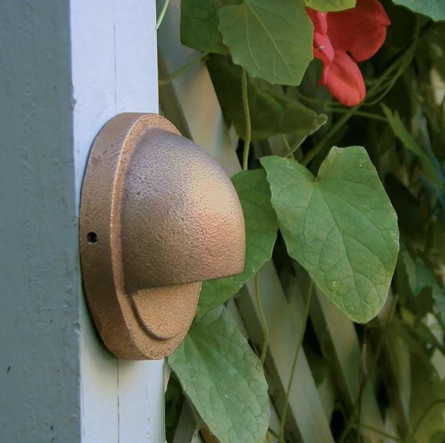Brass circular light on a grey post fence next to leaf with red flower.