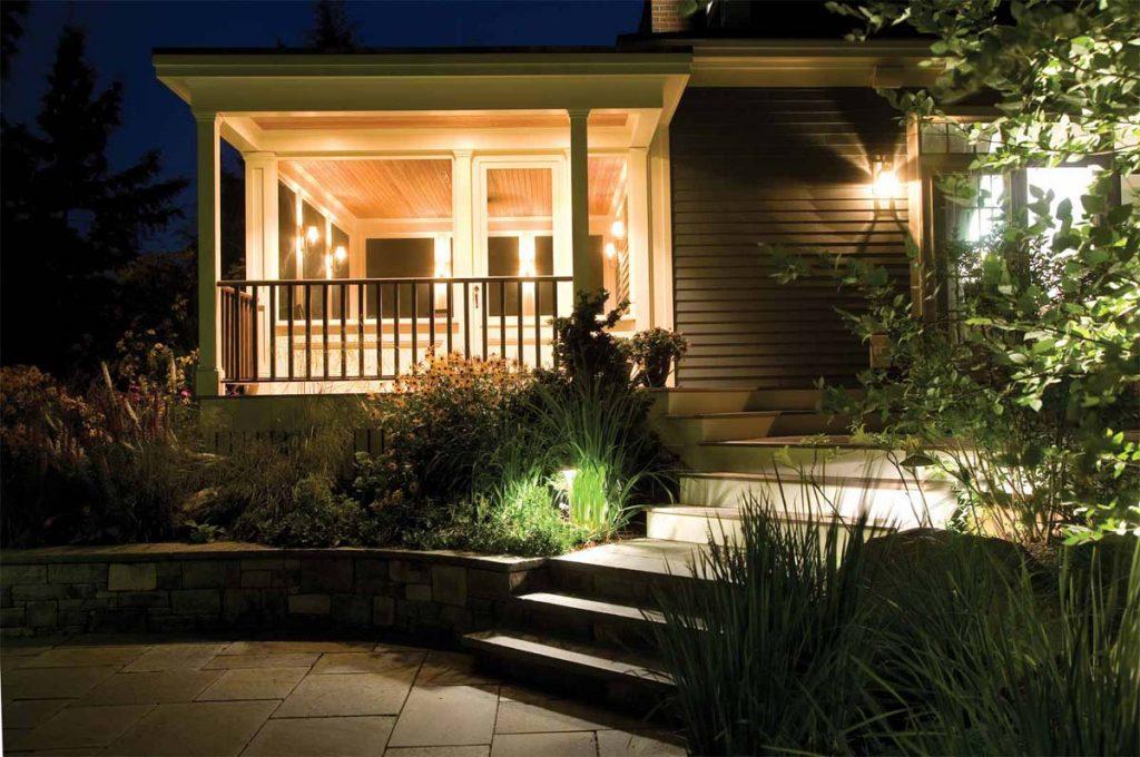 Lit up porch with step lights in grass along the side of steps at night.