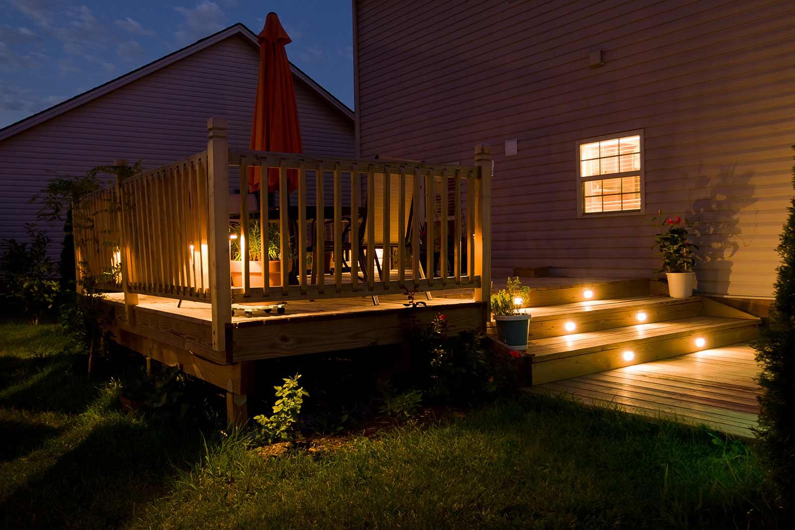 Wooden deck with step lights illuminating stairs and upper patio at night.