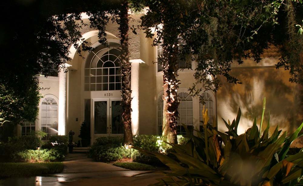 Landscape lighting of palm tress in the front of a white house