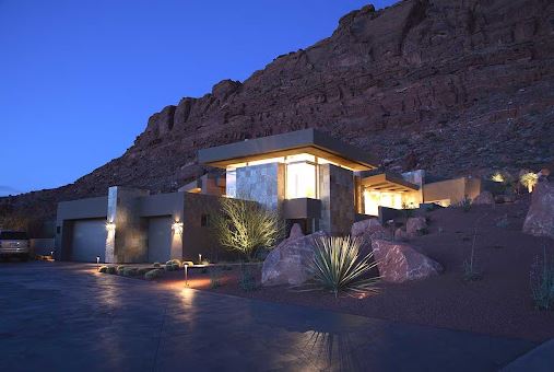A contemporary house with pathway lights and downward-facing wall lights next to the garage door in front of a well-lit main house.