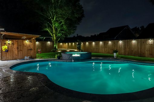 Circular pool water lit up at night with lights hanging from a wooden fence around it.