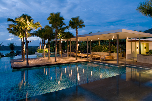 Lit up pool at dusk with home patio attached and illuminated palm trees.